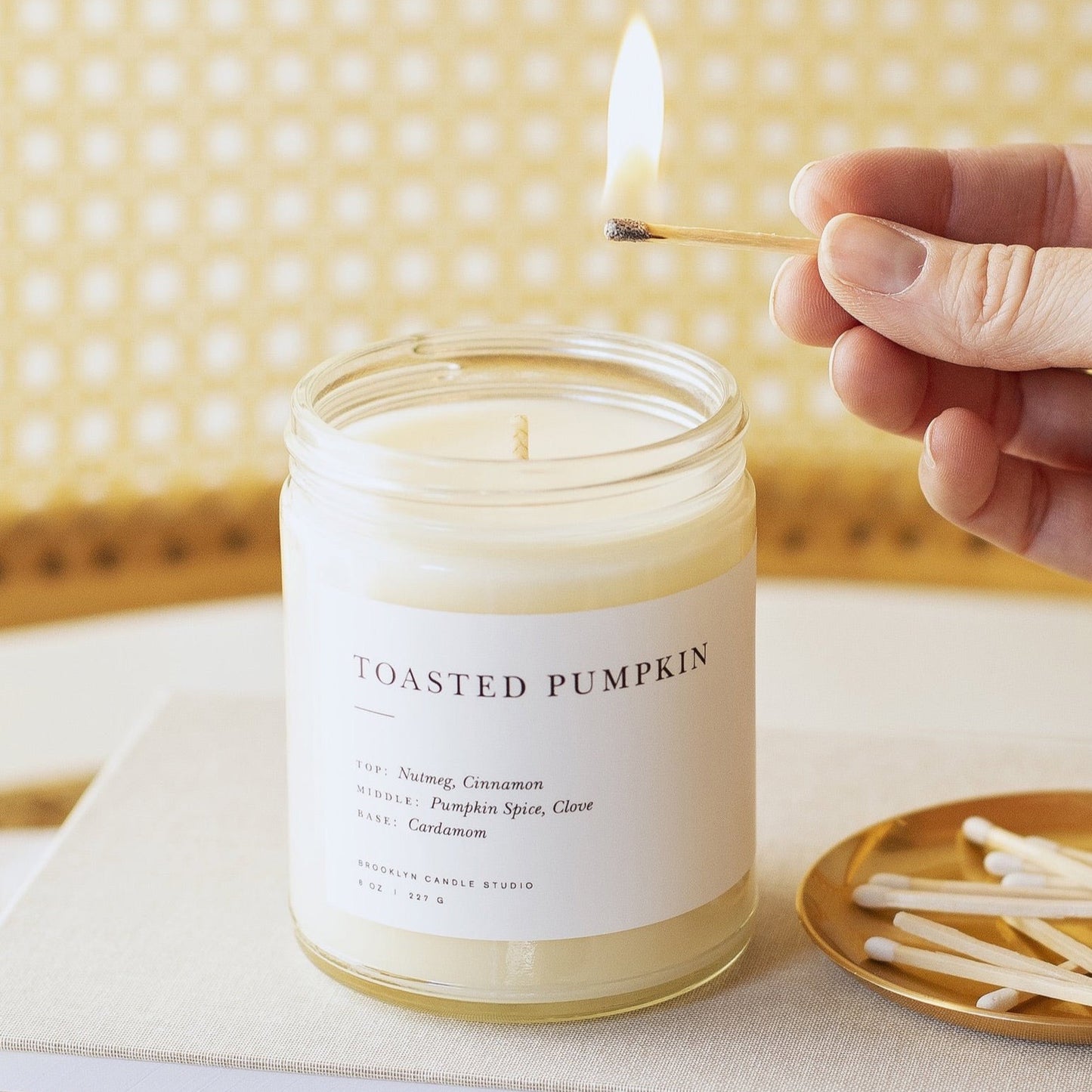 Toasted Pumpkin Brooklyn Candle on top of a book with a lit match held above to light it