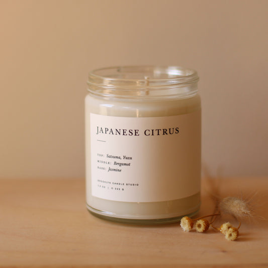 Japanese Citrus Brooklyn Candle with lid off and small flowers laying next to it