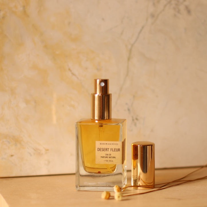 bottle of desert fleur perfume uncapped with gold cap next do it against beige marble wall